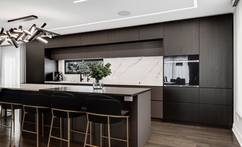 Dark wood kitchen with a black island, brass-legged stools and a sculptural linear light fitting.