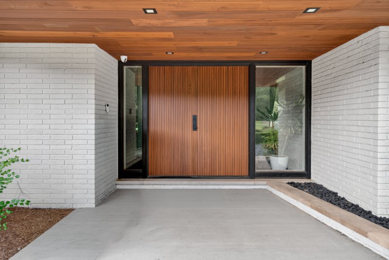 Custom Mahogany entry door with a slatted front, set between glass panels in a white brick entry.