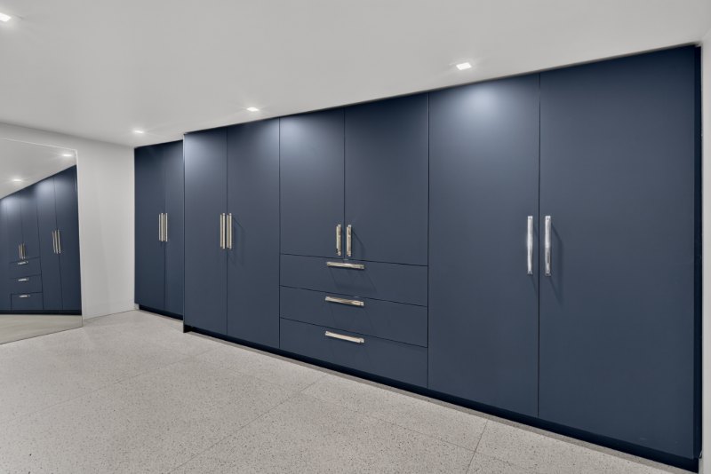 Full-height, wardrobe-style mudroom cabinetry in a deep blue matte finish with long metal pulls.