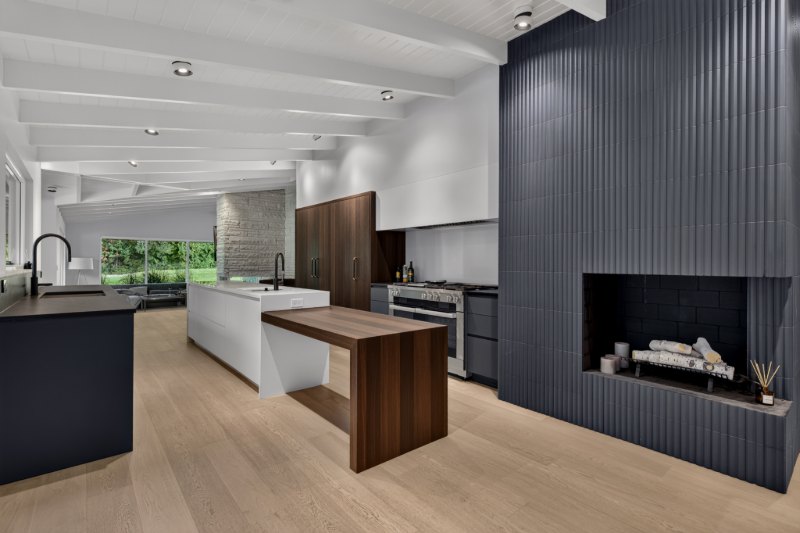 A custom fumed oak table meeting the white island, with dark graphite cabinetry at the range and along the sink wall.