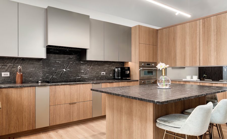 Pale wood and grey kitchen cabinetry with dark stone counters and a full-height stone backsplash.