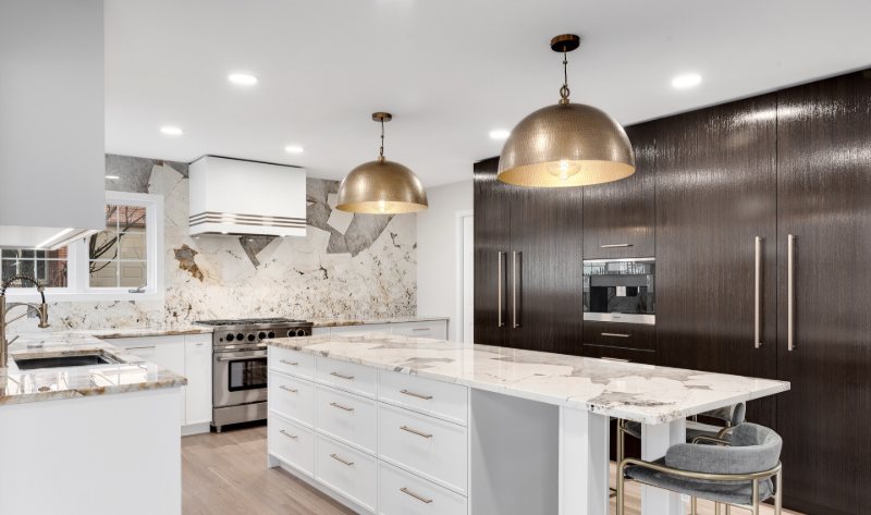 Kitchen with dark full-height wood cabinetry, a white island with stone counters, a veined stone backsplash and brass pendant lighting.